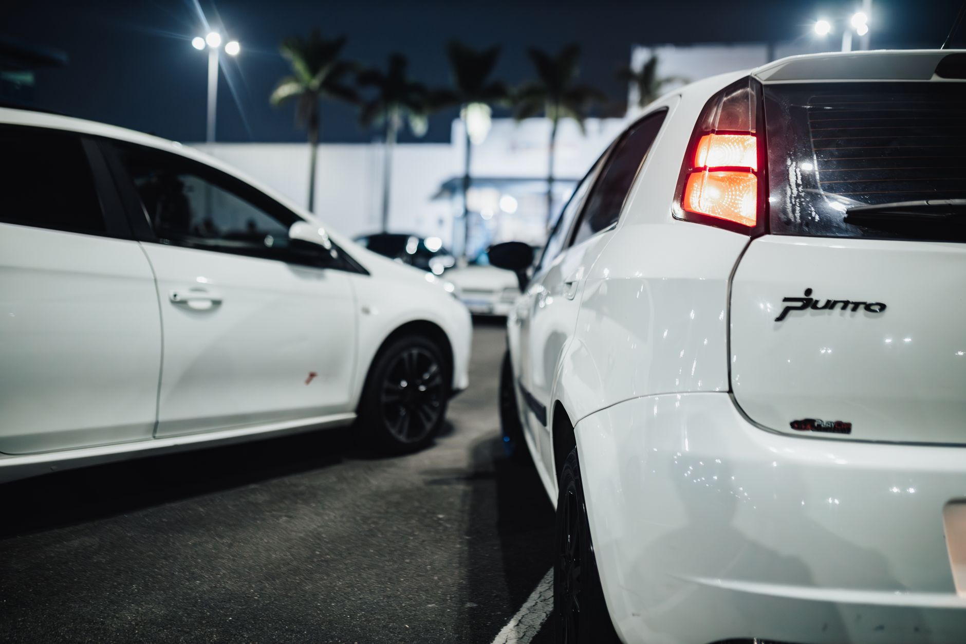 Close-up of white cars parked at night under streetlights in an urban setting.